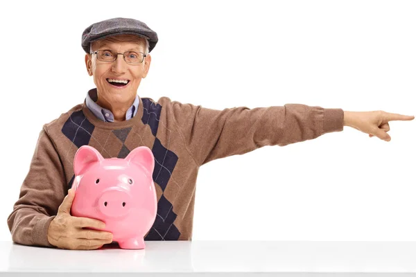 Senior med en piggybank pekar just på en tabell — Stockfoto