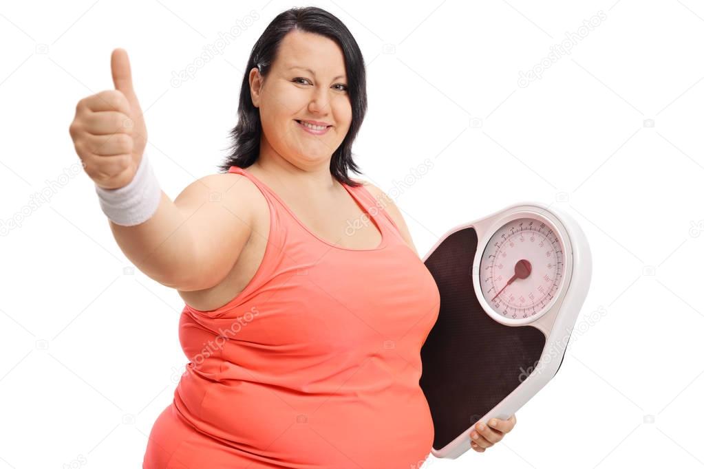 Overweight woman with weight scale making thumb up sign