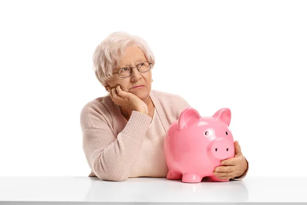 Pensive woman with a piggybank seated at a table — Stock Photo, Image