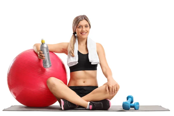 Mulher com uma bola de pilates e uma garrafa sentada em um tapete de exercício — Fotografia de Stock