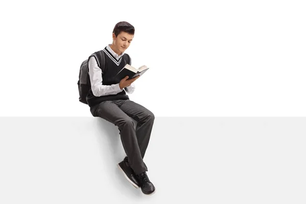Teenage student sitting on a panel and reading a book — Stock Photo, Image