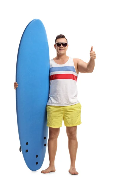 Homem segurando uma prancha de surf e fazendo um gesto polegar para cima — Fotografia de Stock