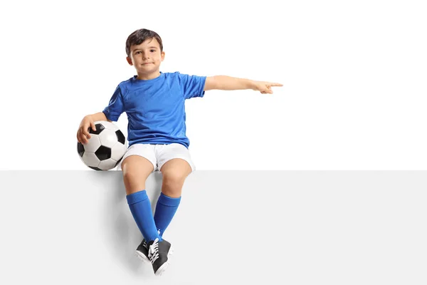 Mały piłkarz siedzi na panelu i wskazując — Zdjęcie stockowe