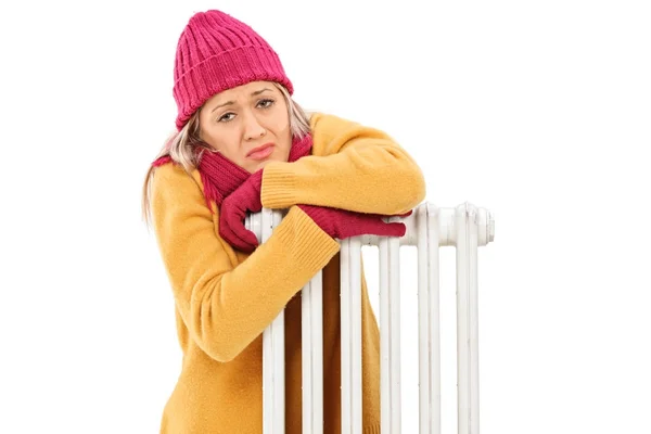 Freezing young woman leaning on a radiator — Stock Photo, Image