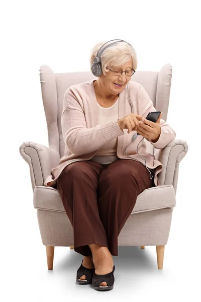 Woman listening to music on a phone in an armchair — Stock Photo, Image
