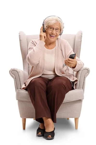 Mulher ouvindo música em um telefone em uma poltrona — Fotografia de Stock