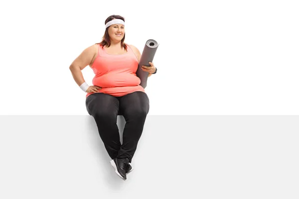 Femme en surpoids avec un tapis d'exercice assis sur un panneau — Photo