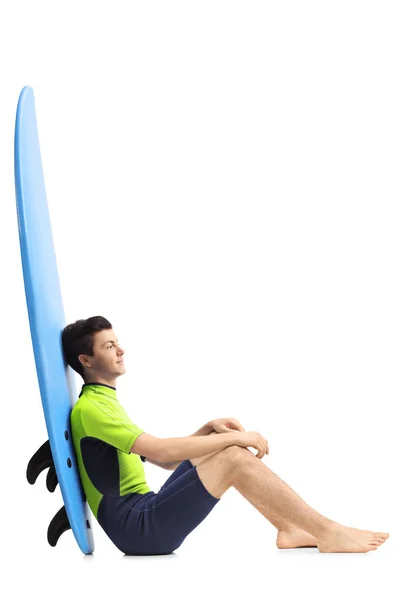 Surfer sitting on the floor and leaning on a surfboard — Stock Photo, Image