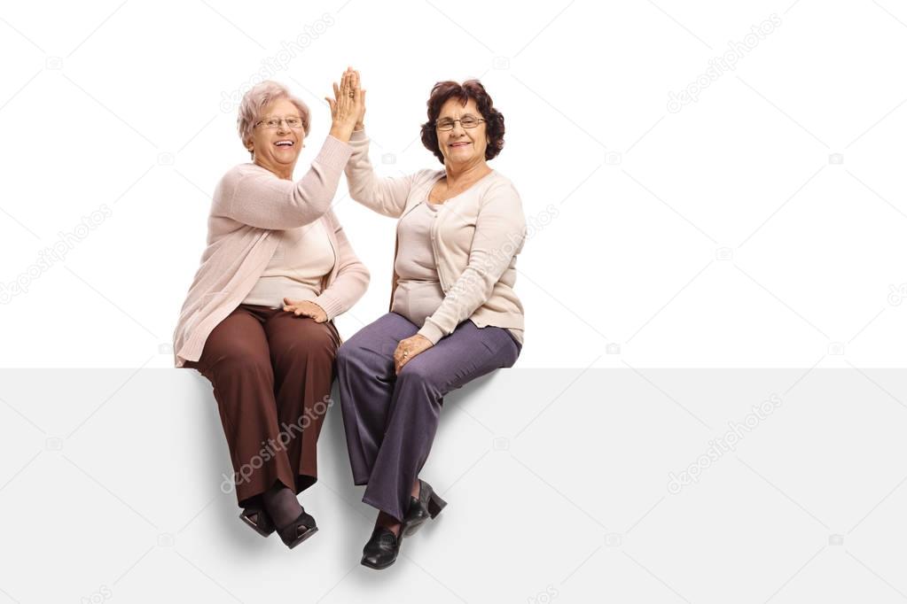 women seated on a panel high-fiving each other