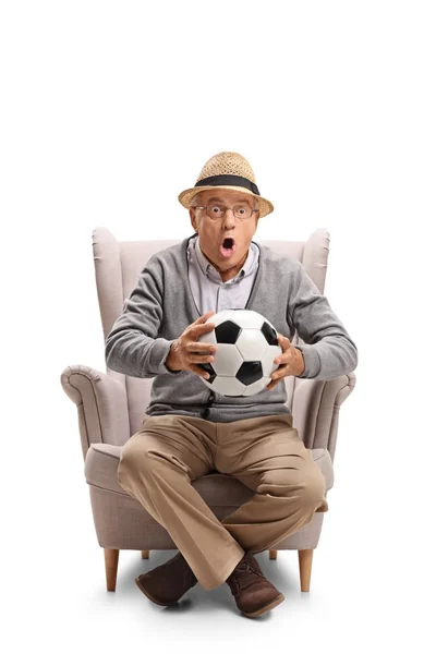 Hombre sosteniendo un balón de fútbol y sentado en un sillón — Foto de Stock