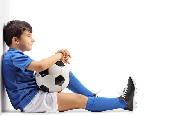 Fundersam liten fotbollsspelare som sitter på golvet — Stockfoto