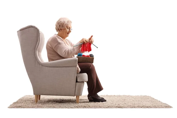 Senior lady sitting in an armchair and knitting — Stock Photo, Image