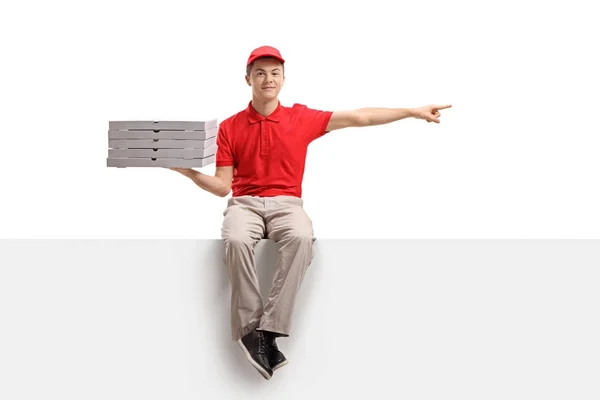 Pizza delivery boy sitting on a panel and pointing — Stock Photo, Image