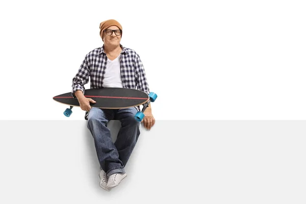 Velho hipster com um longboard sentado em um painel — Fotografia de Stock