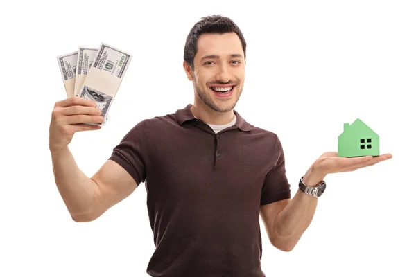 Hombre sosteniendo paquetes de dinero y una casa modelo —  Fotos de Stock