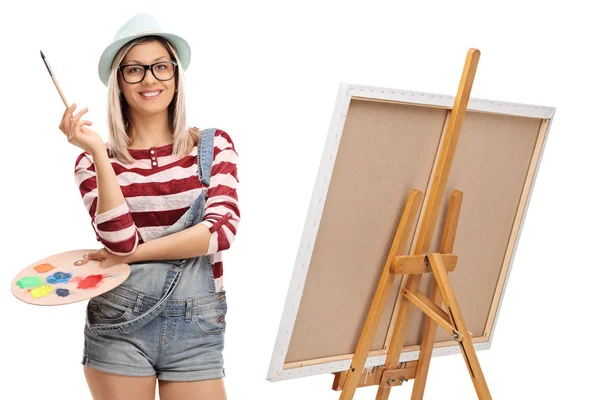 Mulher com um pincel e uma paleta de cores ao lado de um cavalete — Fotografia de Stock