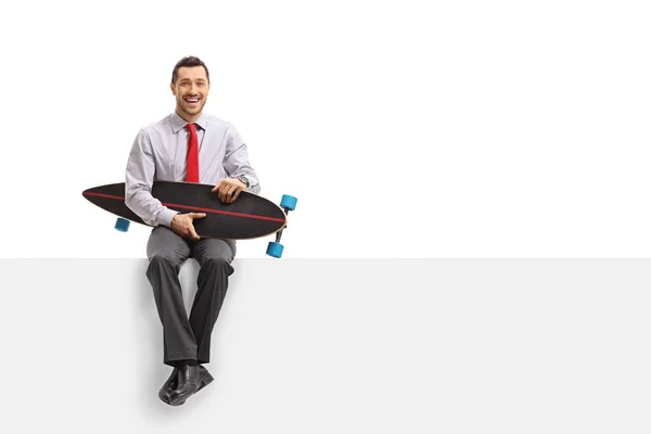 Zakenman met een longboard zitten op een paneel en glimlachen — Stockfoto