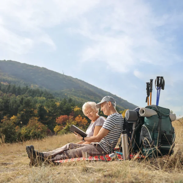 Elderly hikers reading a book outdoors — Stock Photo, Image