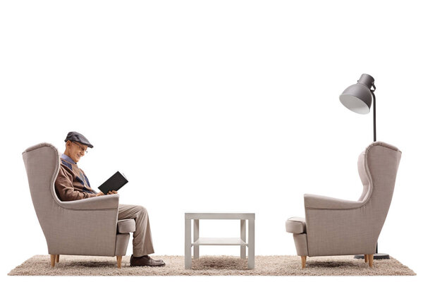 Mature man sitting in an armchair and reading a book isolated on white background