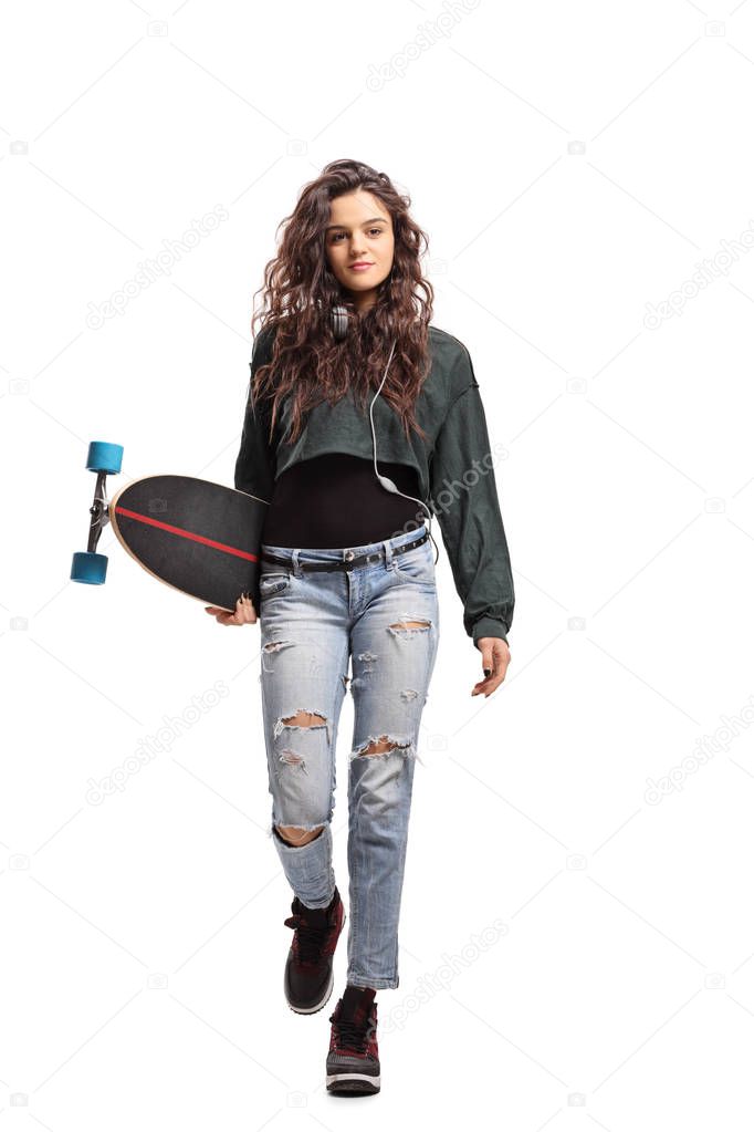 Full length portrait of a teenage girl with a longboard walking towards the camera isolated on white background