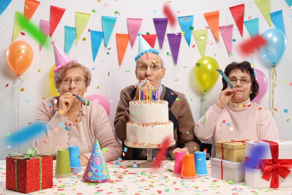 Mayores celebrando un cumpleaños con un pastel y cuernos de fiesta 2023