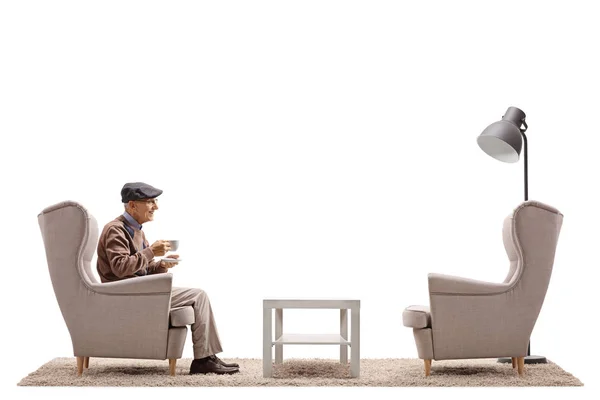 Ένας ηλικιωμένος άνδρας με ένα κύπελλο που κάθεται σε μια πολυθρόνα — Φωτογραφία Αρχείου