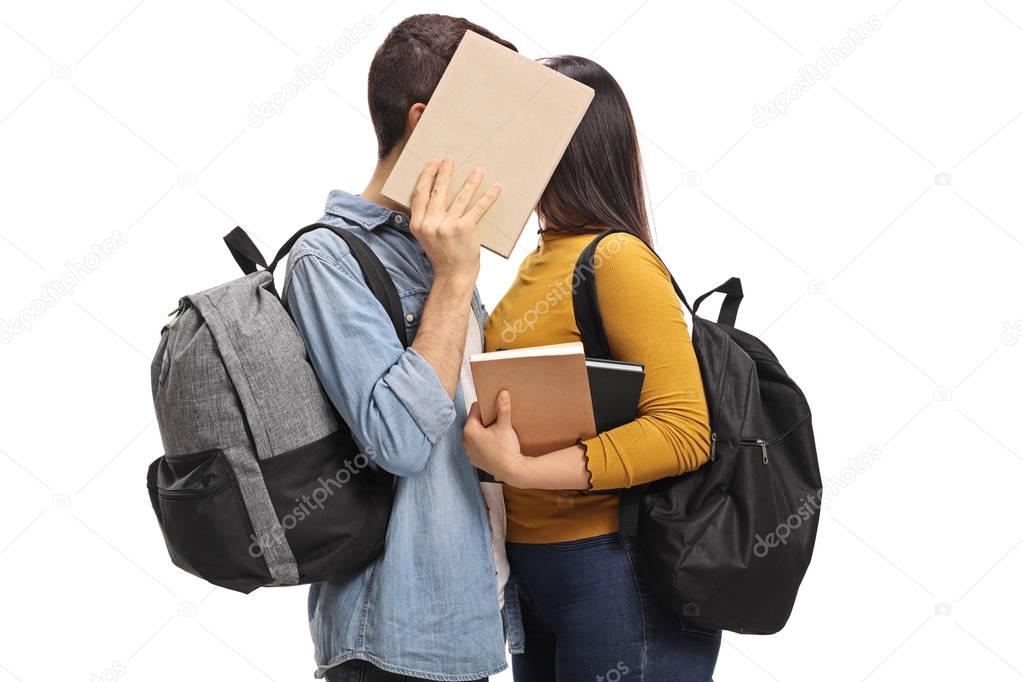 Teen students kissing behind a book
