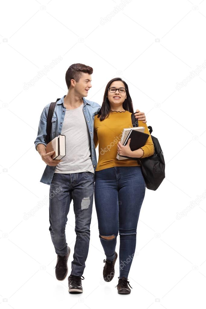 Full length portrait of two teenage students with books and backpacks walking isolated on white background