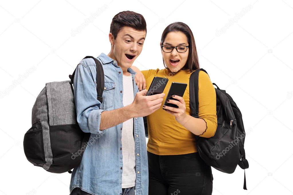 Joyful teenage students looking at phones isolated on white background