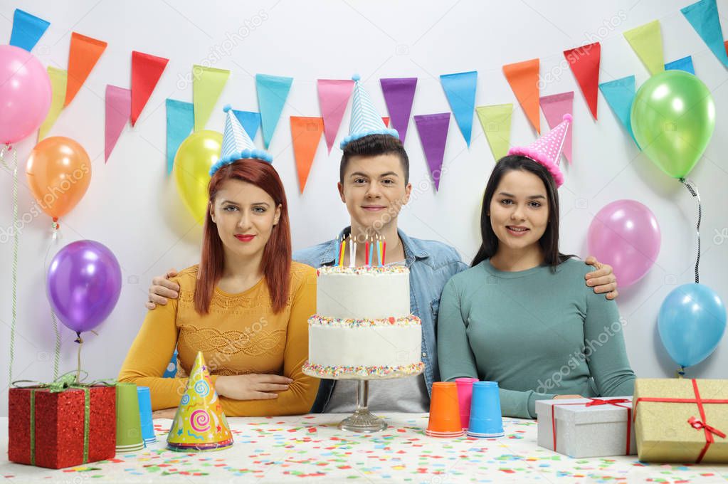 Teenagers with party hats and a birthday cake against a wall with decorations
