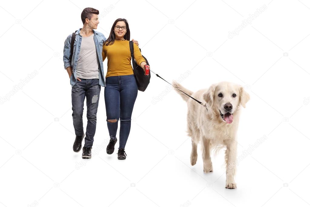 Full length portrait of teenage students walking a dog isolated on white background