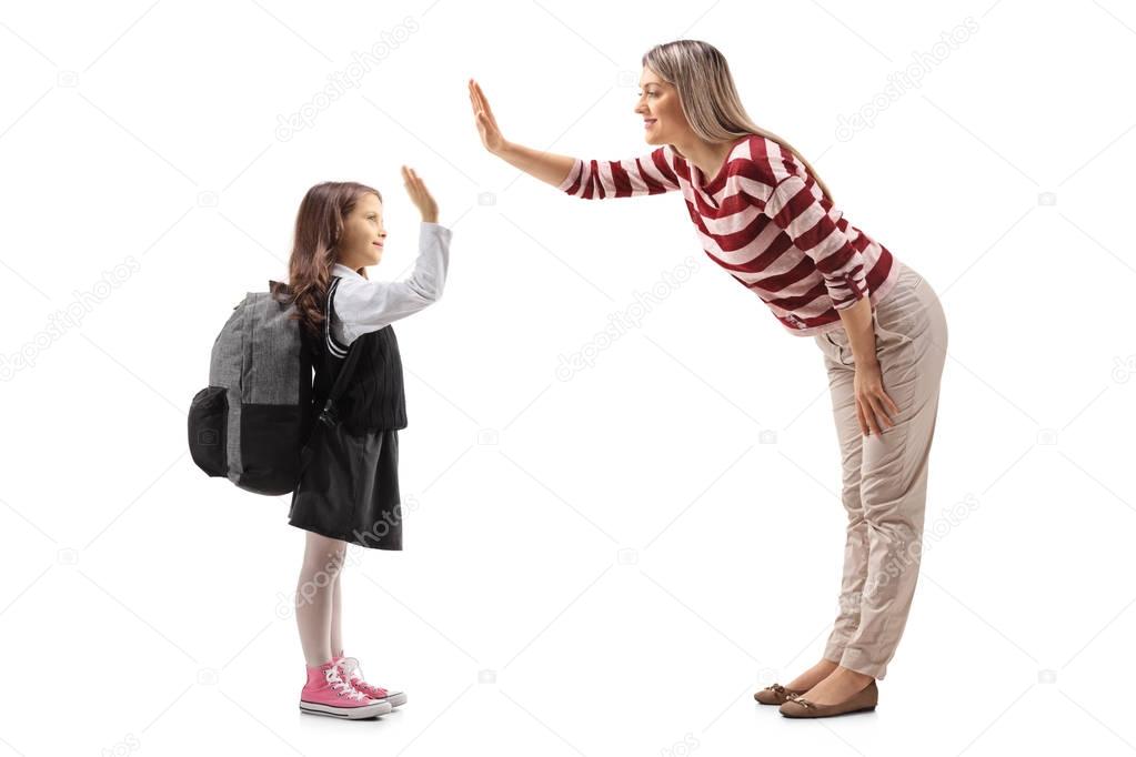 Full length profile shot of a little schoolgirl high-fiving with a young woman isolated on white background