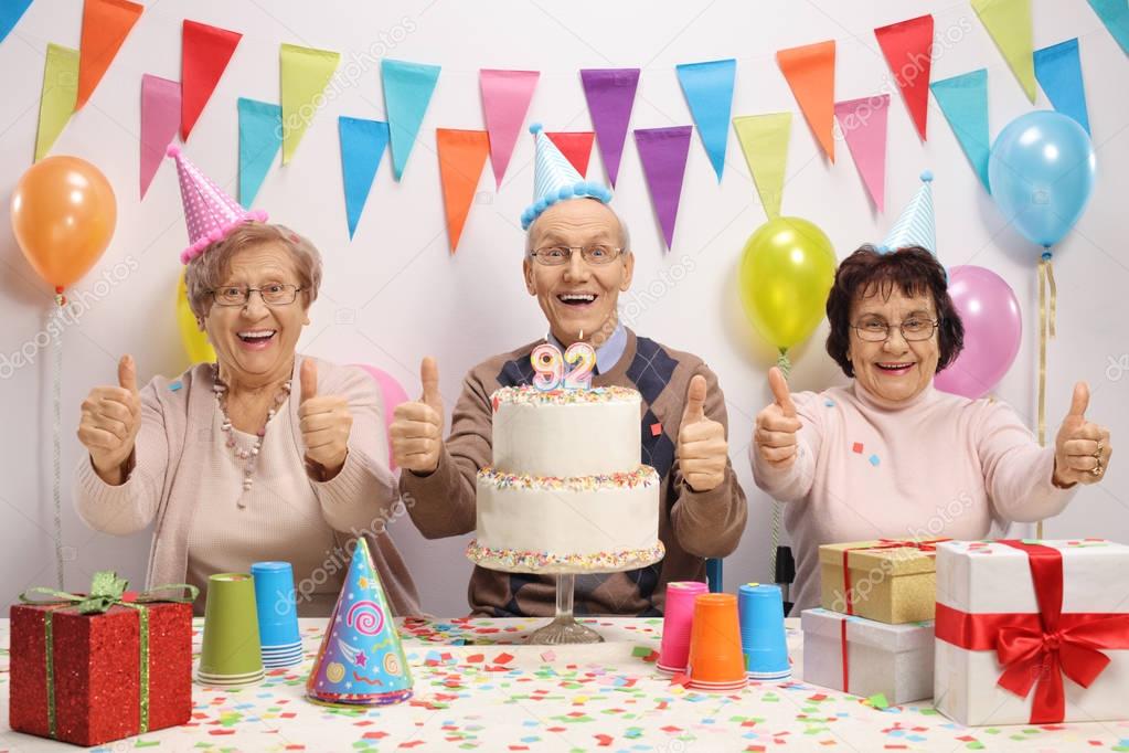 Joyful seniors celebrating a birthday and holding their thumbs up