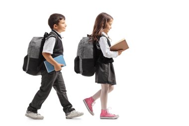 Full length profile shot a schoolboy and a schoolgirl with backpacks and books walking isolated on white background clipart