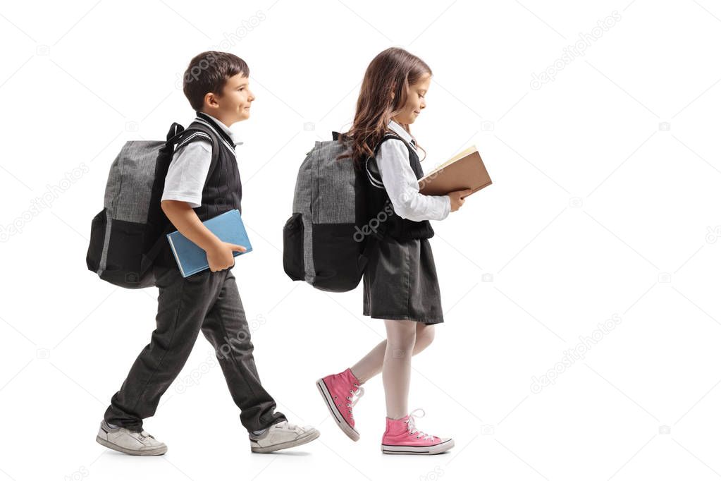 Full length profile shot a schoolboy and a schoolgirl with backpacks and books walking isolated on white background