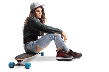 Beyaz arka plan üzerinde izole bir longboard üzerinde oturan genç kaykaycı kız