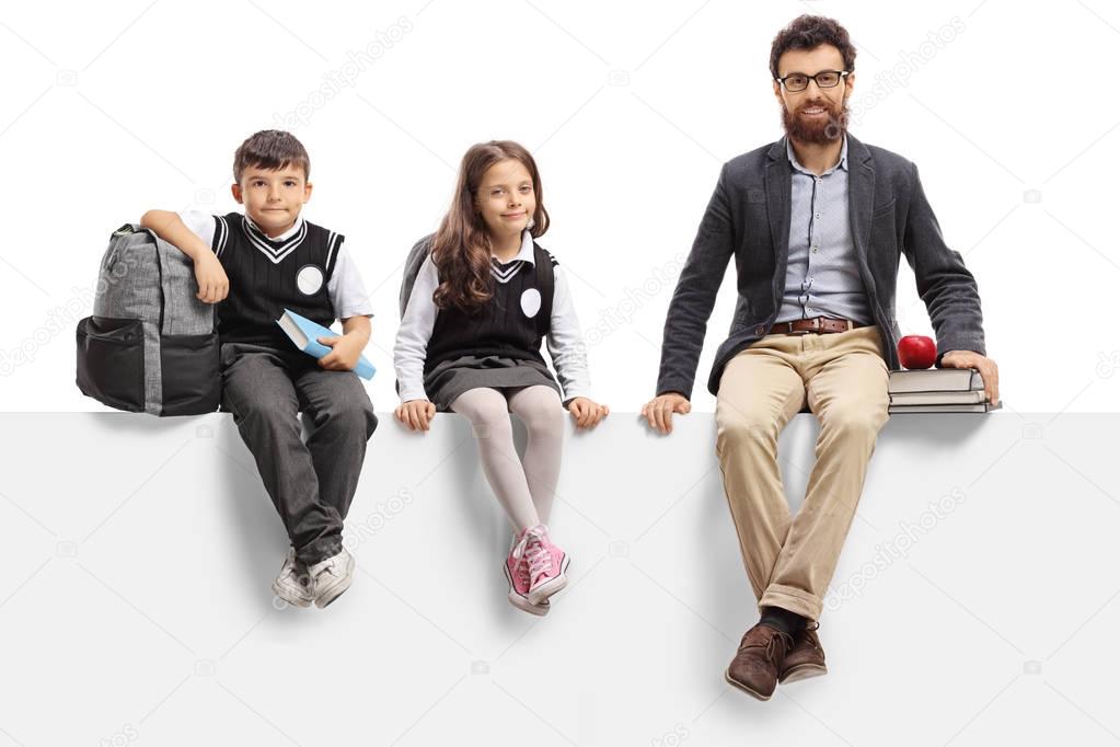 Schoolboy, schoolgirl and a teacher sitting on a panel isolated on white background