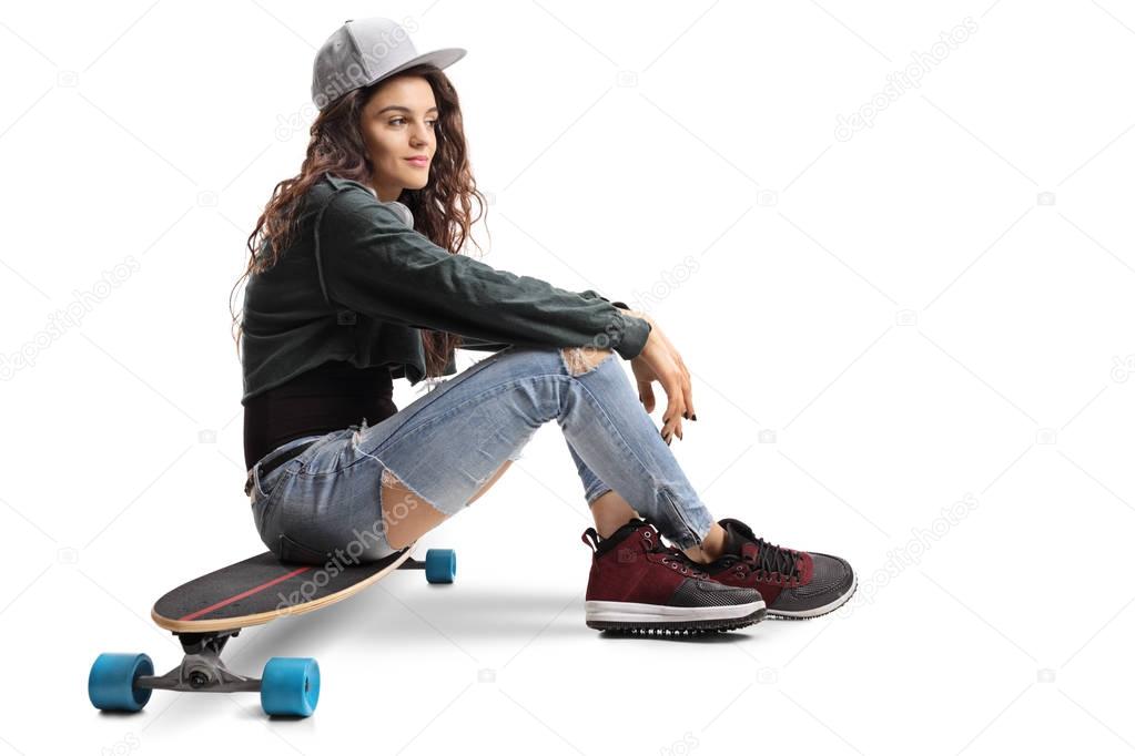 Teenage skater girl sitting on a longboard isolated on white background