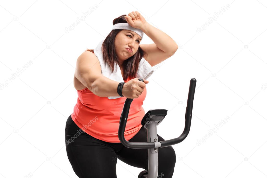 Tired overweight woman exercising on a cross-trainer machine isolated on white background