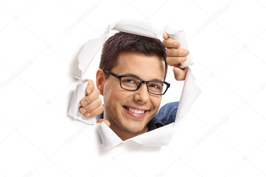 Young guy peeping through a paper hole and smiling isolated on white background