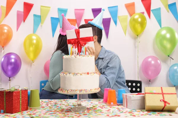 代のカップルが誕生日パーティーで現在の後ろにキス — ストック写真