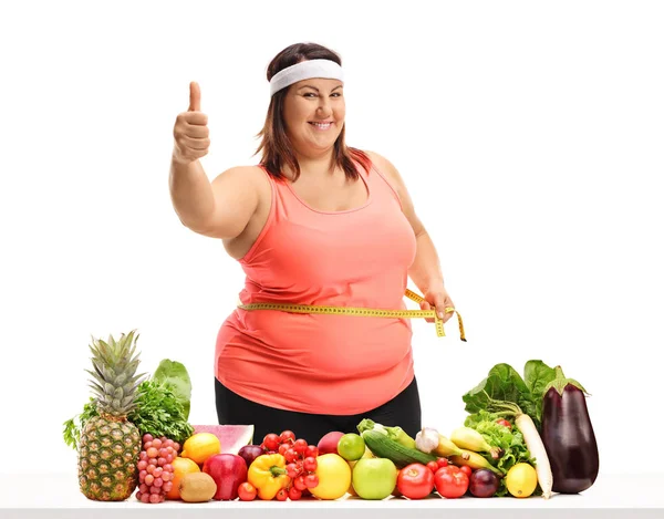 測定測定テープとジェスチャの果物や野菜は 白い背景で隔離のテーブルの後ろを親指を作る腰の肥満女性 — ストック写真