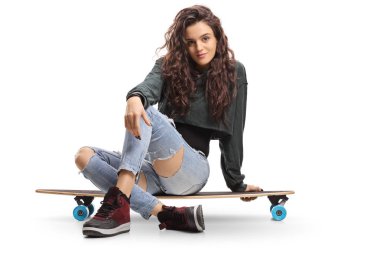 Beyaz arka plan üzerinde izole bir longboard üzerinde oturan patenci kız