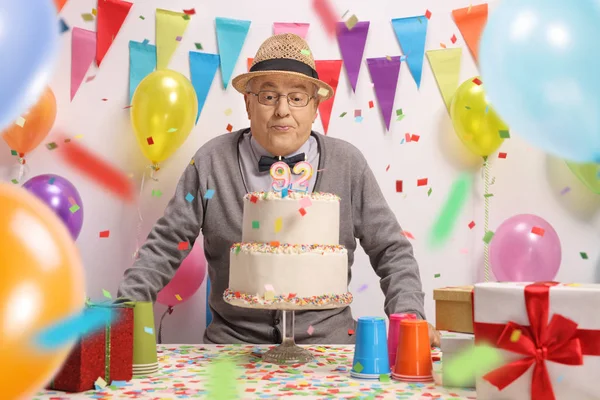 Elderly man blowing candles on a birthday cake with confetti streamers flying around him