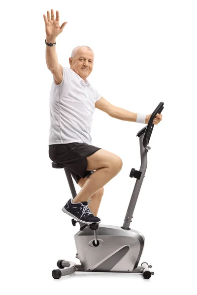 Mature Man Riding Exercise Bike Waving Camera Isolated White Background — Stock Photo, Image