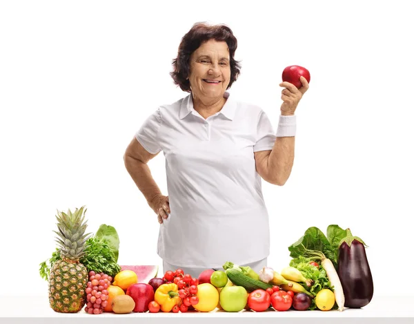 老妇人拿着一个苹果在桌子后面 水果和蔬菜被隔离在白色背景上 — 图库照片