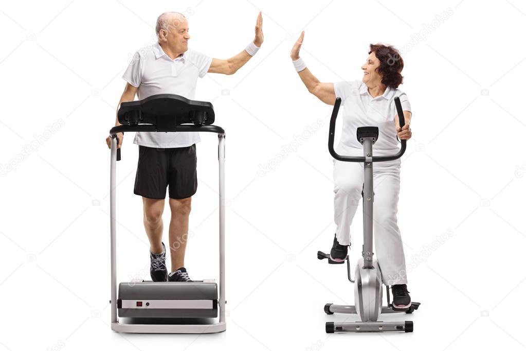 Full length profile shot of an elderly man and an elderly woman exercising and high-fiving each other isolated on white background