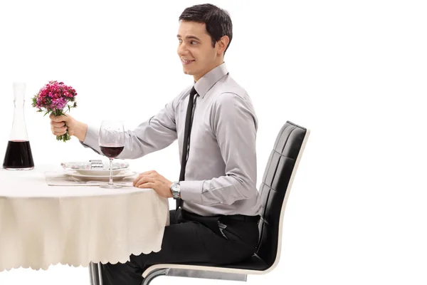坐在餐桌上的年轻人拿着一束花 在白色的背景上被隔绝了 — 图库照片