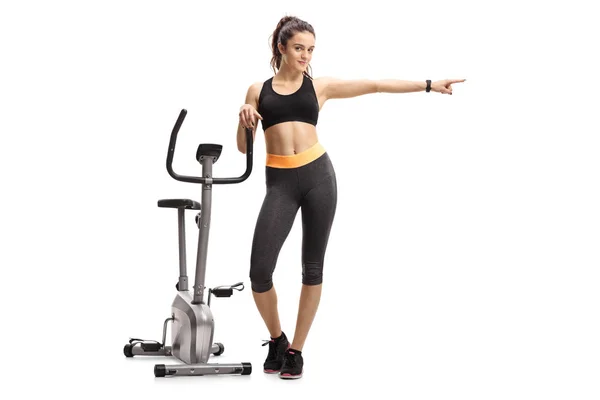 Full Length Portrait Fitness Woman Leaning Exercise Bike Pointing Isolated — Stock Photo, Image