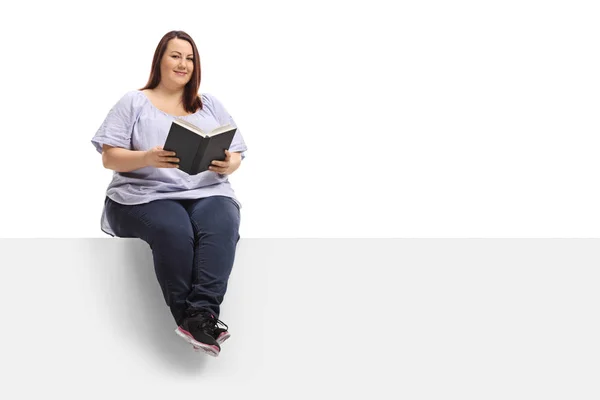 本パネルの上に座って 白い背景で隔離のカメラ目線での肥満女性 — ストック写真